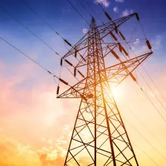 Słupy energetyczne na tle zachodzącego słońca. Zastanawiasz się, ile wynosi odszkodowanie za słupy energetyczne na działce?