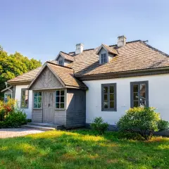 Urokliwa działka siedliskowa z białym domem, drewnianym gankiem i bujną zielenią.