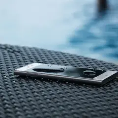 Telefon z kroplami wody na ekranie, leżący na plecionej powierzchni obok basenu. To dowód, że ip68 co oznacza – pełną ochronę przed wodą.