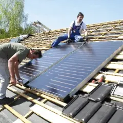 Dwóch mężczyzn montuje panele **solary** na dachu. Jeden pochyla się nad panelami, drugi siedzi obok.