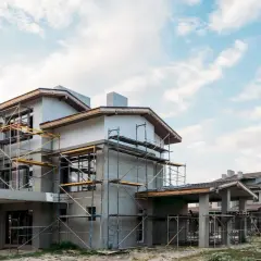 Budowa domu energooszczędnego taniego w budowie. Konstrukcja z rusztowaniami, nowoczesna architektura, jasne niebo z chmurami.