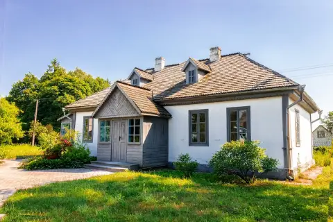 Urokliwa działka siedliskowa z białym domem, drewnianym gankiem i bujną zielenią.