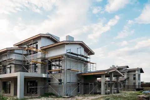 Budowa domu energooszczędnego taniego w budowie. Konstrukcja z rusztowaniami, nowoczesna architektura, jasne niebo z chmurami.