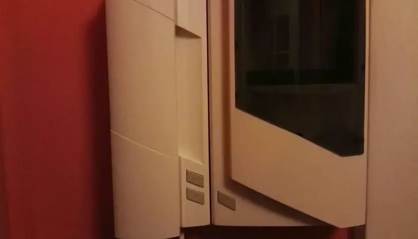 Biały unifon zamontowany na czerwonej ścianie. Urządzenie ma prosty, nowoczesny design z ciemną szybką.