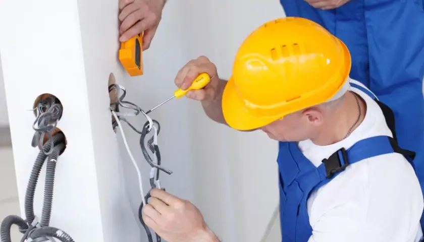 Elektryk w żółtym kasku pracuje przy instalacji, zastanawiając się, ile zarabia elektryk w Norwegii.