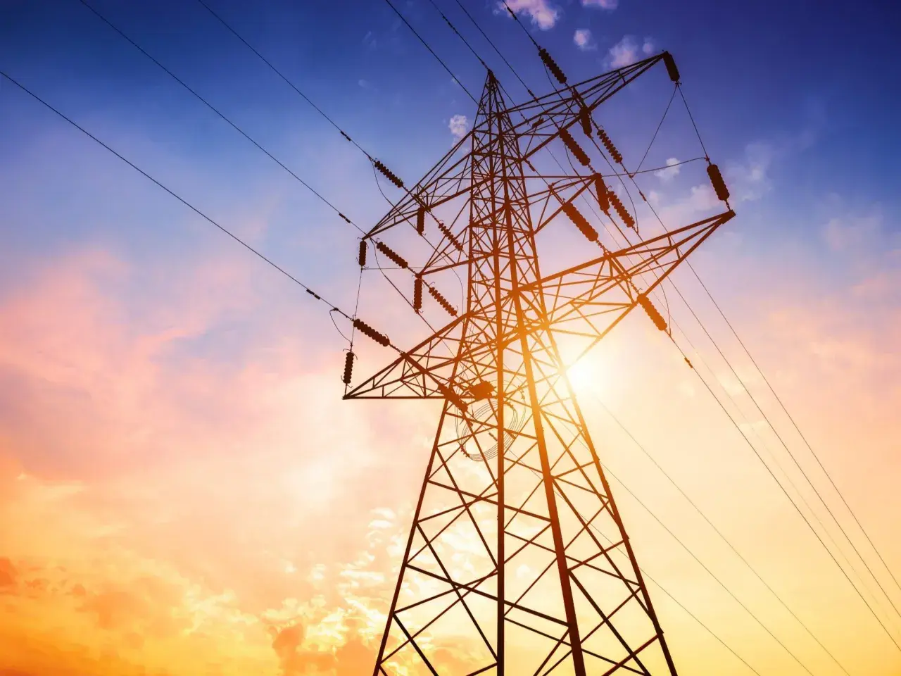 Słupy energetyczne na tle zachodzącego słońca. Zastanawiasz się, ile wynosi odszkodowanie za słupy energetyczne na działce?