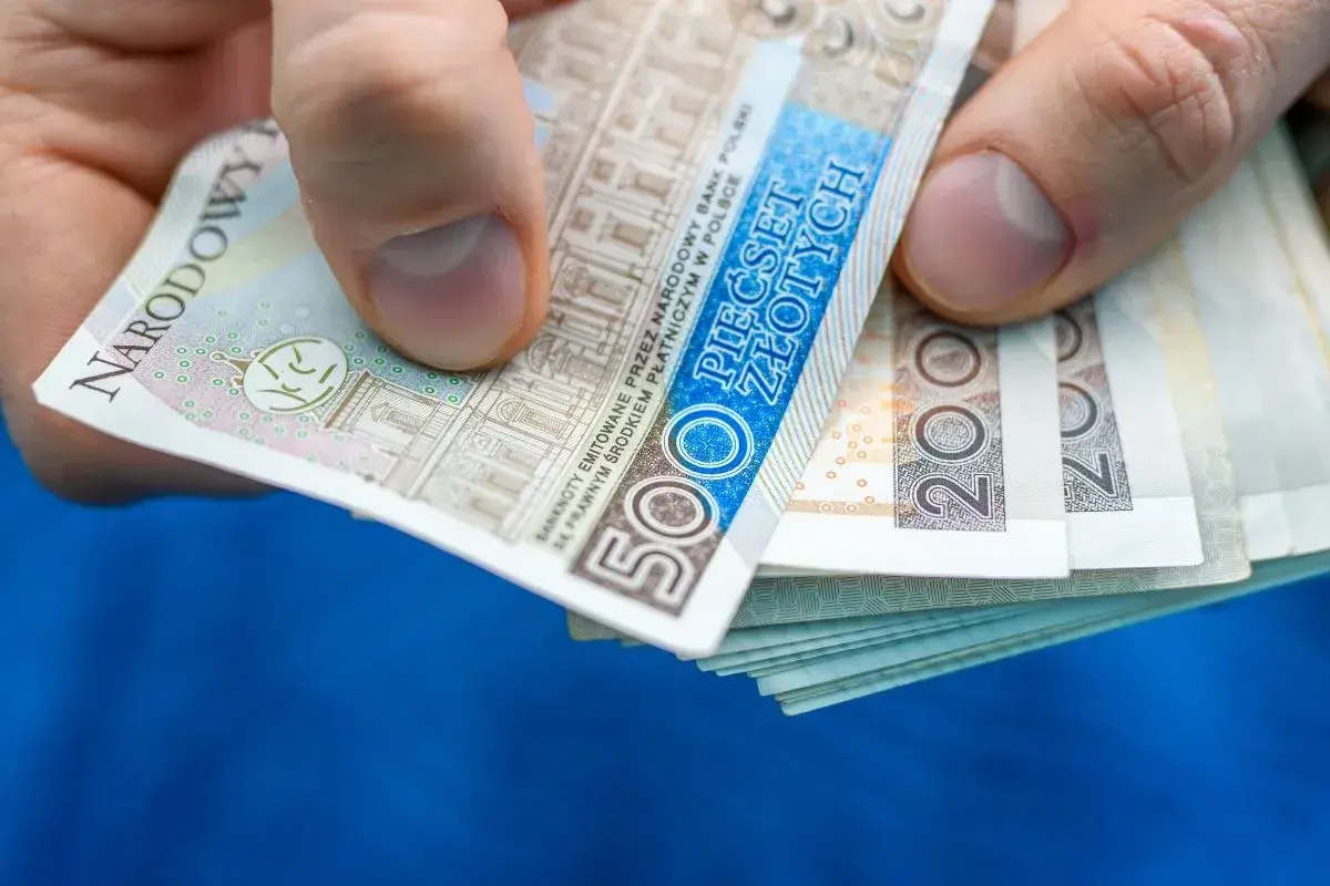 Dłoń trzyma stos banknotów 500 zł i 200 zł. Może to być zapłata za rachunek, np. taryfa urzędowa Energa.