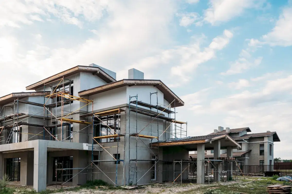 Budowa domu energooszczędnego taniego w budowie. Konstrukcja z rusztowaniami, nowoczesna architektura, jasne niebo z chmurami.