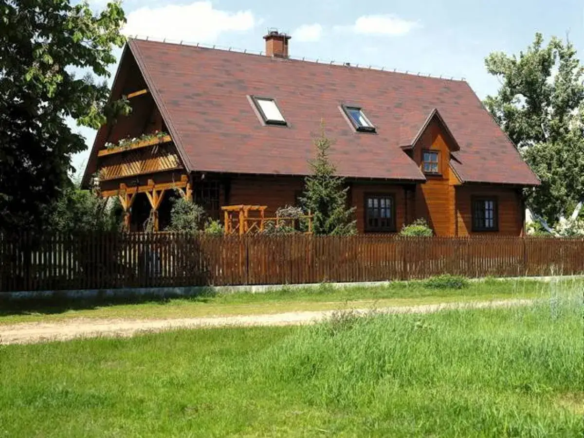 Drewniany dom z werandą i balkonem, otoczony płotem. Idealna działka siedliskowa na spokojne życie.