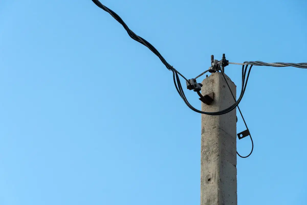Betonowy słup energetyczny na działce, z którego zwisają kable.