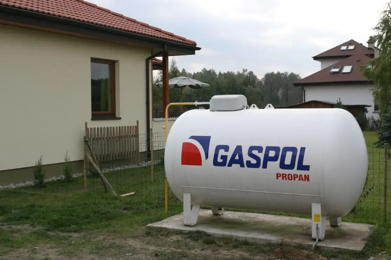 Biały zbiornik na propan z logo GASPOL stoi obok domu.